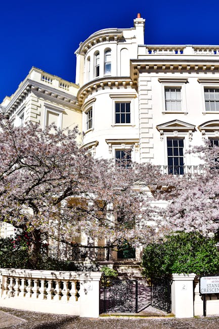 A close-up view of a large, elegant white residential building with classical architectural features including rounded bay windows, decorative cornices, and a curved façade set against a clear blue s